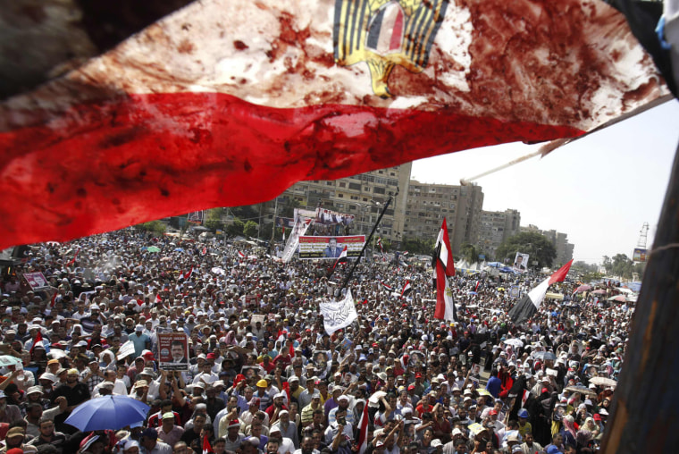 Image: An Egyptian flag stained with blood flutters over members of the Muslim Brotherhood and supporters of deposed Egyptian President Mursi during a protest outside Raba El-Adwyia mosque in Cairo