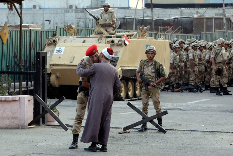 Image: A religious scholar kisses an army officer as a greeting before talking to him in front of the Egyptian museum where Egyptian army soldiers stand guard in Cairo