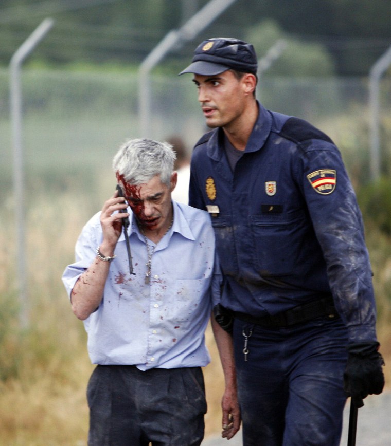 Image: An injured passenger is helped by a policeman after a train crashed near Santiago de Compostela