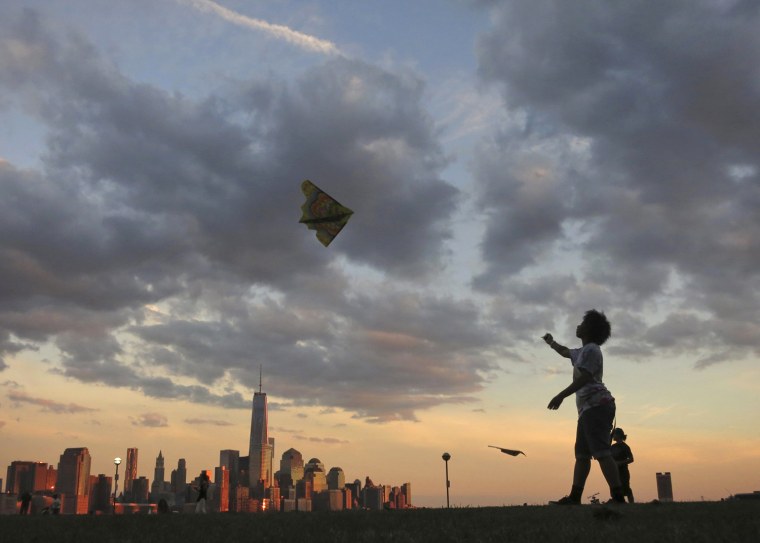 Image: A woman flies a kite in front of the skyline of New York's Lower Manhattan and One World Trade Center in a park along the Hudson River in Hoboken