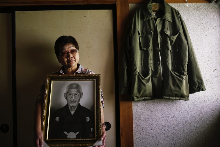 Image: Mieko Okubo, 59, poses with a portrait of her father-in-law Fumio Okubo next to his jacket in his room where he committed suicide in the evacuated town of Iitate in Fukushima prefecture
