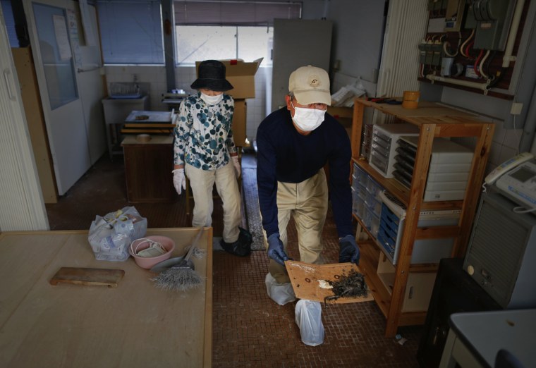 Image: Zenjuro Nagaoka  is followed by his wife Satoko as he takes a dead mouse out of their sweet shop during a visit to the evacuated town of Namie