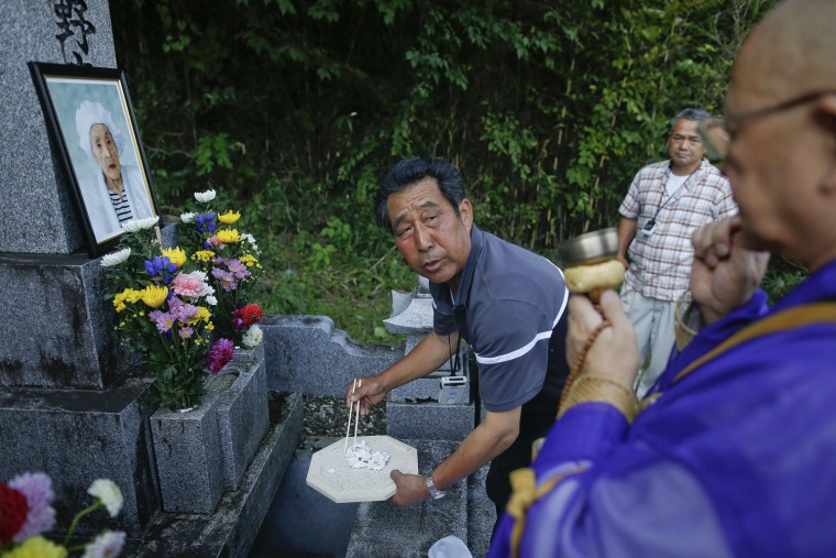 Image: A relative of Yotsuno Kanno uses chopsticks to put her remains into a family grave during a small ceremony at a cemetery in the evacuated town of Minamitsushima