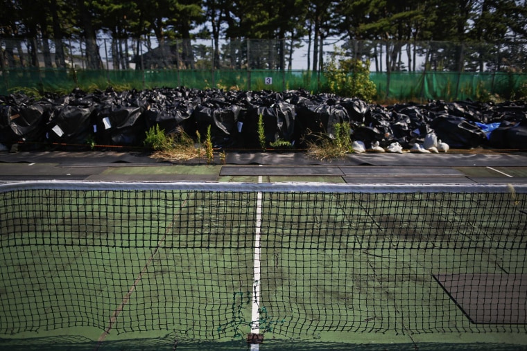 Image: Big plastic bags containing radiated soil, leaves and debris from the decontamination operation are dumped at the tennis court at sports park in Naraha town