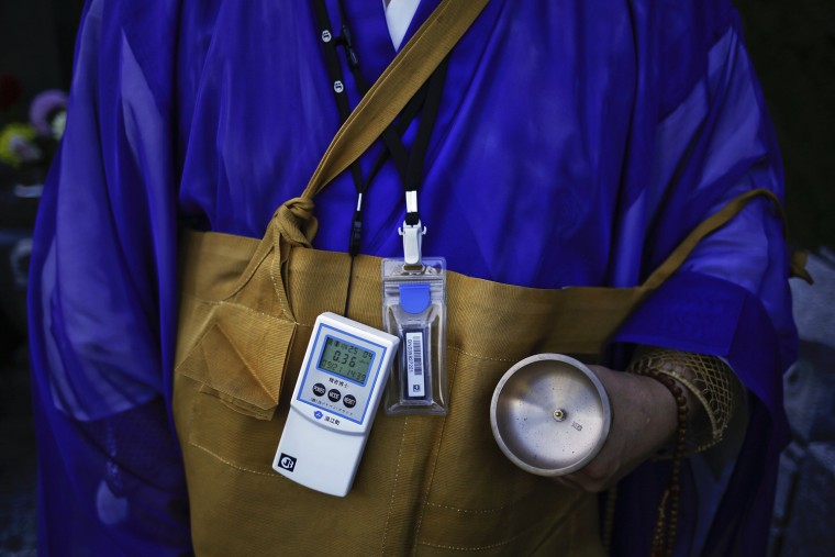 Image: A Buddhist monk wears a Geiger counter as he leads a small funeral ceremony for a woman who died as an evacuee at a cemetery in the evacuated town of Minamitsushima