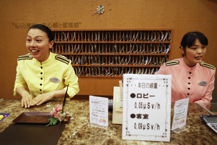 Image: Hotel staff welcome guests behind a sign with levels of radiation at the hotel's lobby and rooms in the Iwaki town