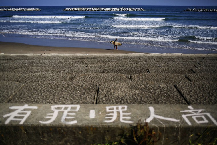 Image: A surfer carries board as others catch waves before anti-tsunami barriers on closed Toyoma beach near Iwaki town, south of the tsunami-crippled Fukushima Daiichi nuclear power plant in Fukushima prefecture