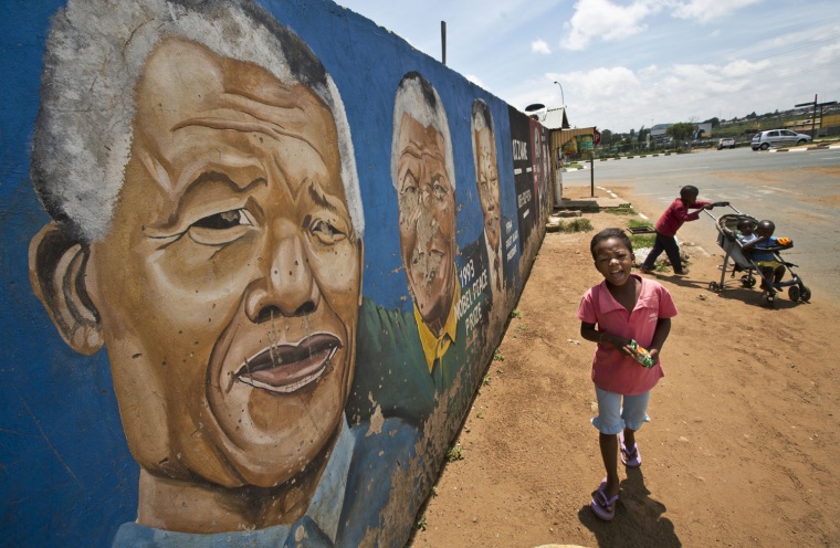 Image: Children walk past a mural depicting Nelson Mandela during different stages of his in Johannesburg on Saturday.