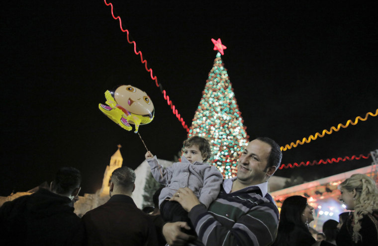 Image: A man holds a child in front of a Christmas tree that was lit during a ceremony outside the Church of Nativity in Bethlehem