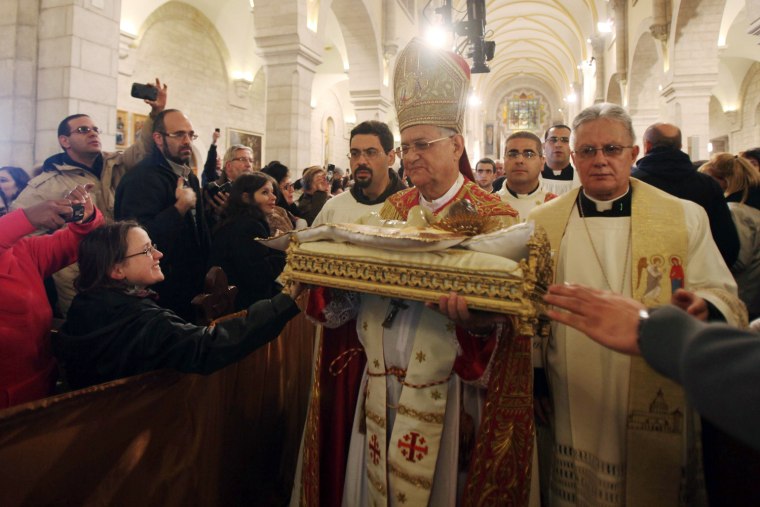 Image: Latin Patriarch of Jerusalem Fouad Twal carries a statuette of baby Jesus during Christmas midnight mass in Bethlehem