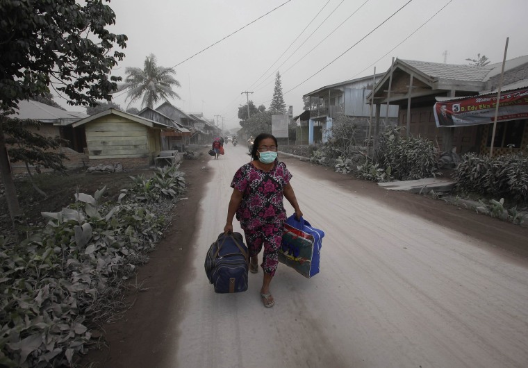 Image: A villager carries her belongings during an evacuation after ash from Mount Sinabung volcano hit Payung village in Karo district