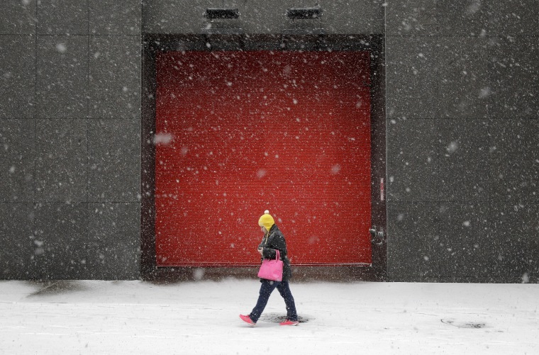 Image: A woman walks outside of an office building as snow falls in Baltimore.