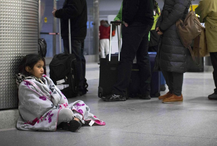 Image: A child sits next to a service line at the John F. Kennedy International Airport in New York