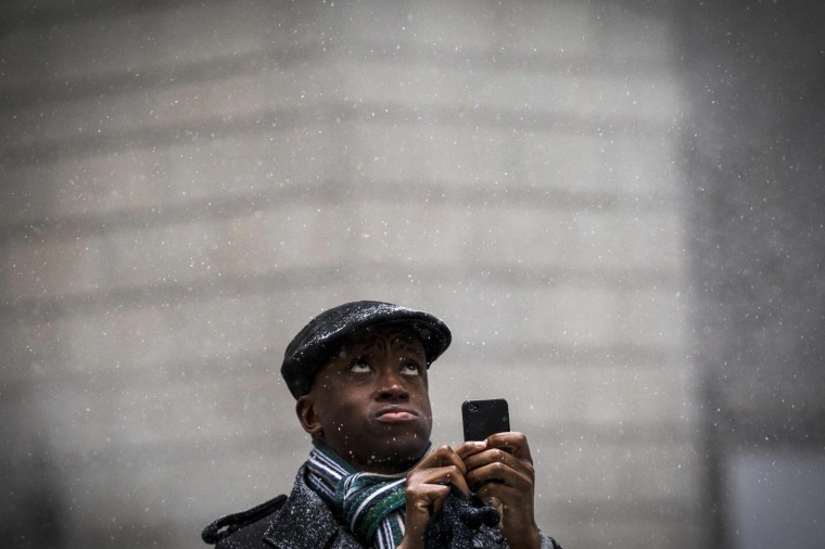 Image: A man takes a picture with his phone during a snow storm in Manhattan's financial district in New York