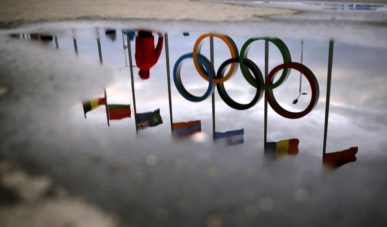 Image: A man walks past the Olympic rings as they are reflected in a puddle of rain water as preparations continue at the Olympic Park for the Sochi 2014 Winter Olympics
