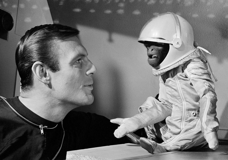 His own space suit, with oxygen tank, doesn't make Barney the monkey any happier as he and actor Adam West view the situation in their space capsule in Hollywood on January 24, 1964.   Barney, a South American woolly monkey, is blasted into space with West, as an astronaut, in a new movie, \"Robinson Crusoe On Mars.\"     (AP Photo)