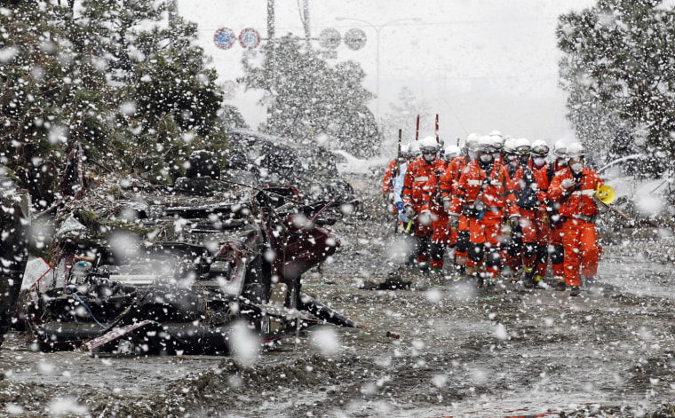 Image: Heavy snow falls on rubble and rescue workers at a devastated factory area hit by an earthquake and tsunami in Sendai, northern Japan