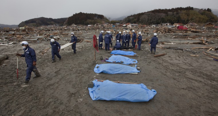 Image: Policemen gather around the covered bodies of victims retrieved from the debris in Rikuzentakata