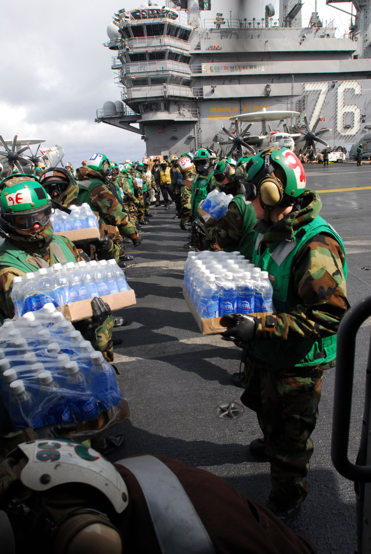 Image: U.S. Navy handout photo of sailors loading a helicopter with bottled water aboard the USS Ronald Reagan