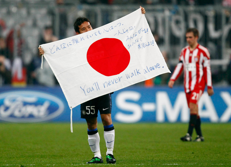 Image: Inter Milan's Yuto Nagamoto of Japan holds a Japanese flag after their Champions League round of 16 second leg soccer match against Bayern Munich in Munich