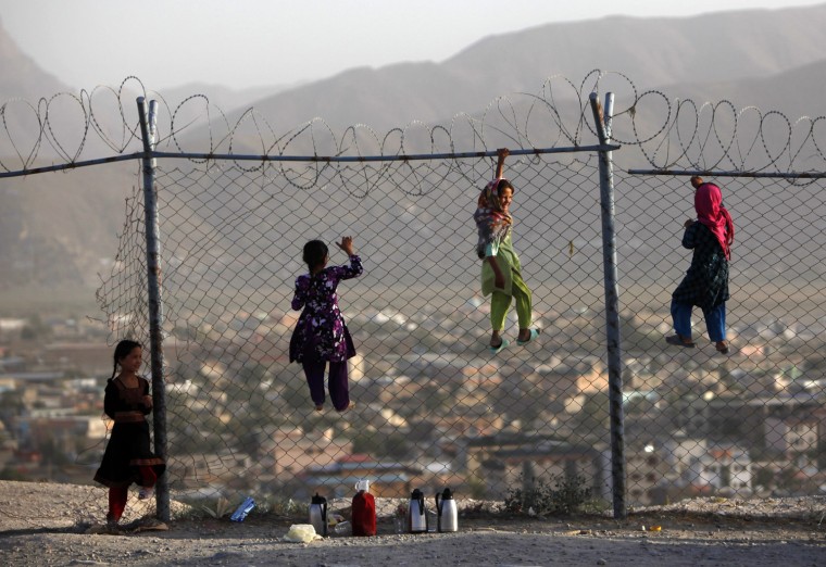 Image: Afghan children climb onto a fence while playing as they sell tea in Kabul