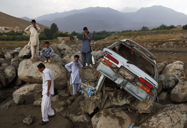 Image: Afghans stand near a destroyed car after floods in the Shakar Dara district of Kabul