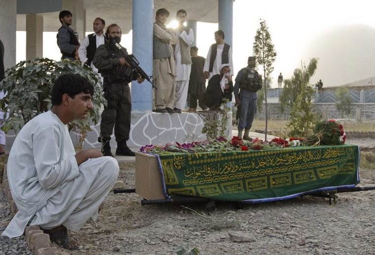 Image: An unidentified relative of Kandahar city mayor, Ghulam Haidar Hamidi, sits next to the coffin Hamidi who was killed after a suicide blast in Kandahar