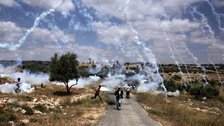 Palestinian demonstrators run for cover as Israeli soldiers fire tear gas during a protest against Israel's controversial separation barrier in the West Bank village of Bilin, near Ramallah, on May 1, 2009. Israel says the projected 723 kilometres (454 miles) of steel and concrete walls, fences and barbed wire is needed for security. The Palestinians view it as a land grab that undermines their promised state. The International Court of Justice (ICJ) issued a non-binding resolution in 2004 calling for parts of the barrier inside the West Bank to be torn down and for construction there to cease. Israel has ignored the ruling. AFP PHOTO/ABBAS MOMANI (Photo credit should read ABBAS MOMANI/AFP/Getty Images)