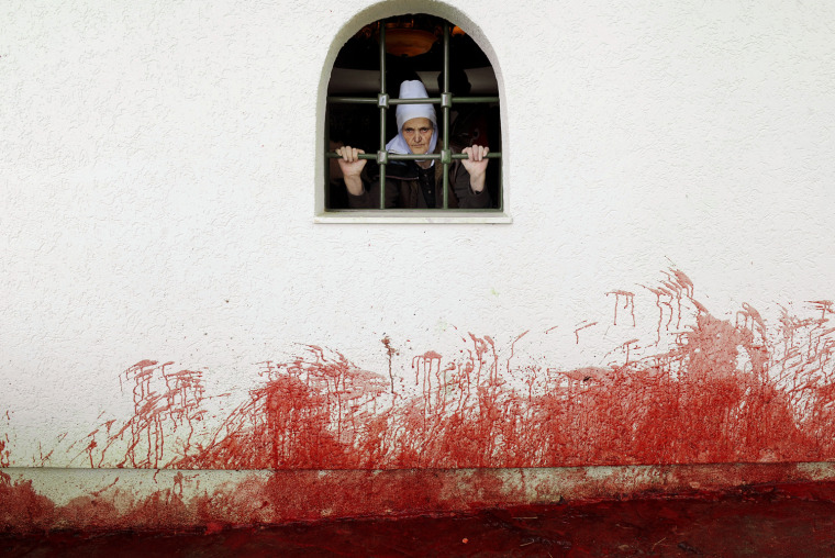 A Kosovo Albanian woman looks out a window in the village of Babaj Bokes after sheep were slaughtered on May 6 2009 during the celebration of the traditional feast of Saint George's Day, which is observed by  several nations, kingdoms, countries, and cities of which Saint George is the patron saint.           AFP PHOTO / ARMEND NIMANI (Photo credit should read Armend Nimani/AFP/Getty Images)