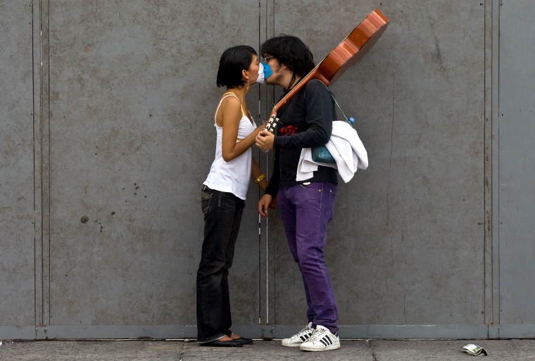 A couple wearing surgical masks to avoid contagion by the influenza A (H1N1) (swine flu virus), kisses at Mexico City's Zocalo square, on April 30, 2009. Mexico on Thursday sharply raised its number of confirmed influenza A (H1N1) (swine flu virus) cases to 260, including 12 deaths, as many citizens prepared to spend the May Day holiday at home to prevent the spread of the virus.  AFP PHOTO/Luis Acosta (Photo credit should read LUIS ACOSTA/AFP/Getty Images)