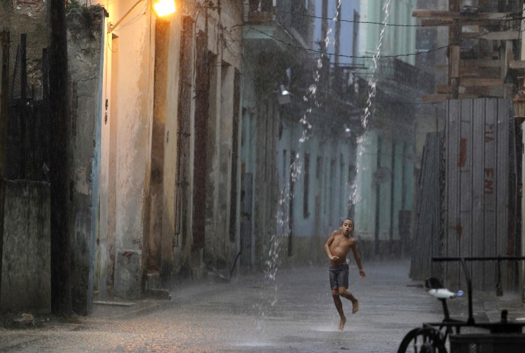 Image: A boy dances in the rain during a heavy tropical shower in a street of Havana