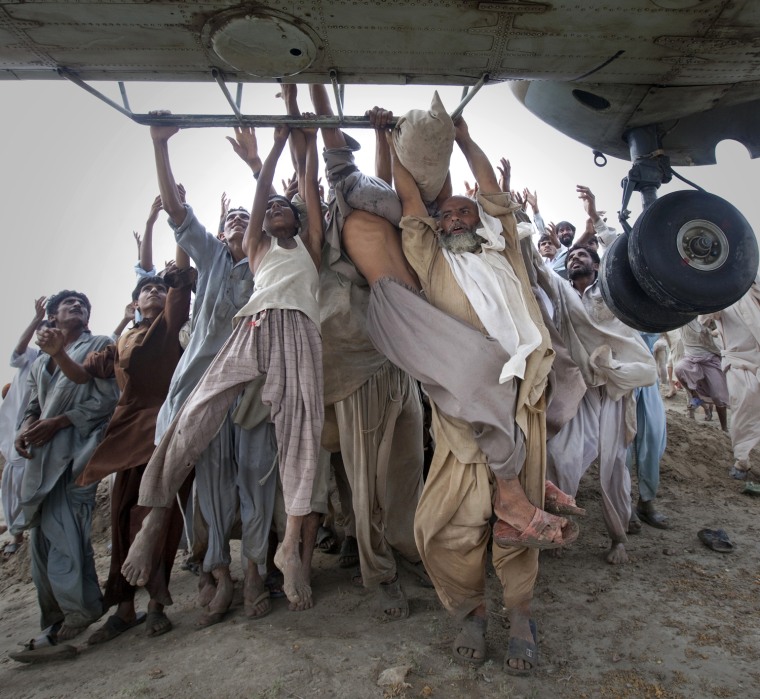 Image: Marooned flood victims looking to escape grab the side bars of a hovering Army helicopter which arrived to distribute food supplies in the Muzaffargarh district of Pakistan's Punjab province