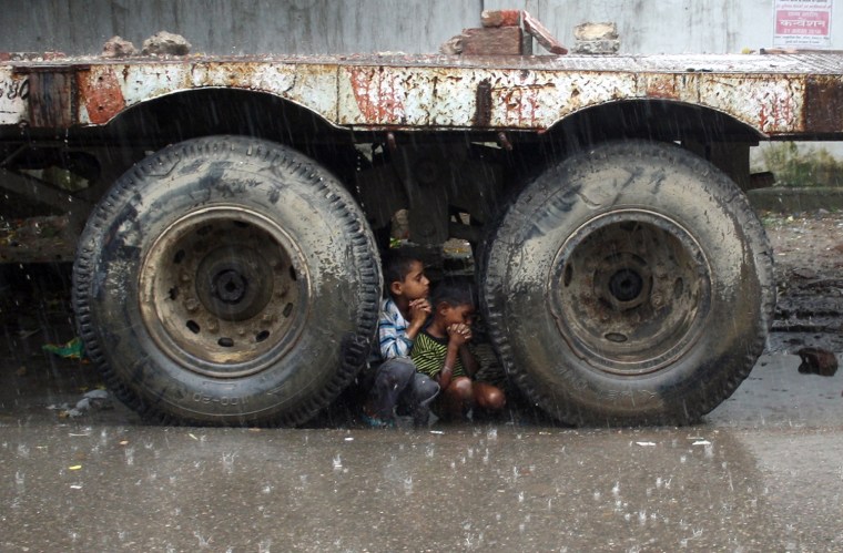 Image: Children take shelter under a trailer during heavy rains in Noida