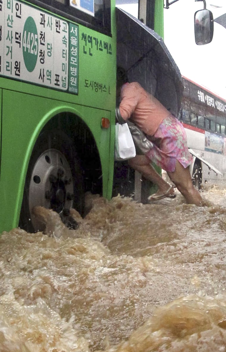 Image: A woman rushes onto a bus on a flooded road during heavy rainfall in Seoul