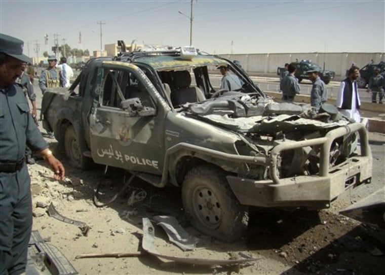 An Afghan police officer, left, looks at a police vehicle damaged in a suicide attack in Lashkar Gah, Helmand province, Afghanistan, Tuesday, Sept. 27, 2011. A suicide bomber rammed a car packed with explosives into a police truck outside a bakery in southern Afghanistan on Tuesday, killing a number of civilians, officials said. (AP Photo/Abdul Khaleq)