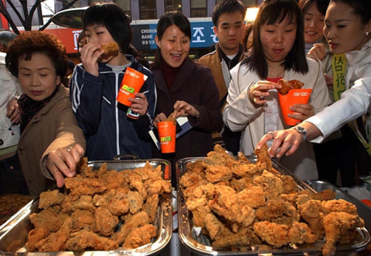 South Korean pedestrians eat free chicken on a street in Seoul Monday. South Korea's poultry industry groups have offered to pay $1.72 million insurance to anyone who gets bird flu from home-bred poultry.