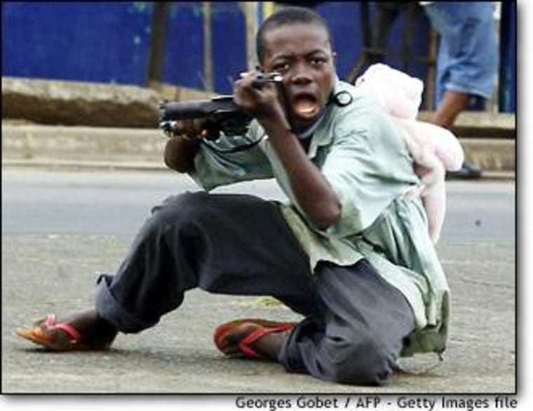 A child soldier wearing a teddy bear backpack points his gun at a photographer in a street of Monrovia on June 27.