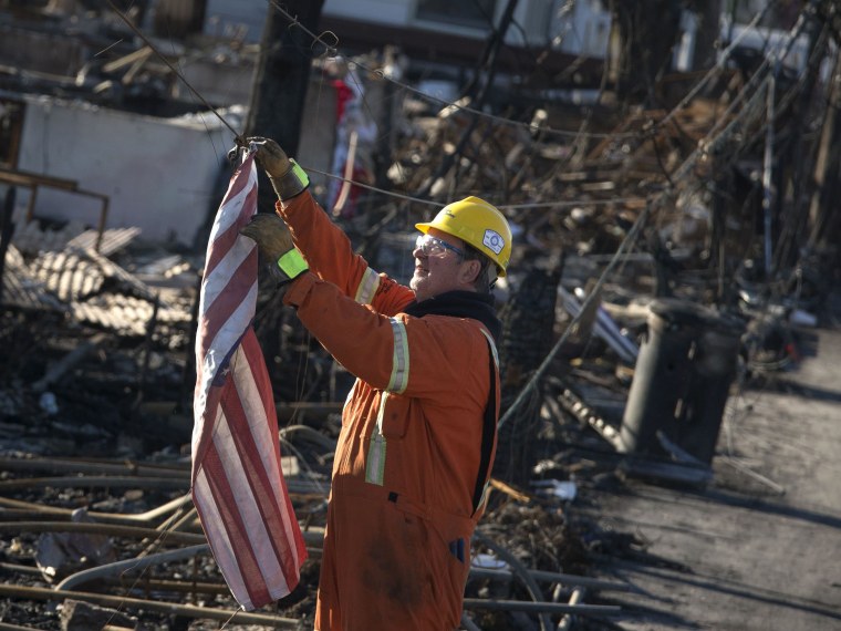 An electrician with Hydro Quebec pulls down a U.S. flag hanging on a cable before testing power lines in Breezy Point neighborhood of Queens. In the worst-hit areas, homes are still without light or heat. (Photo by Adrees Latif/Reuters)