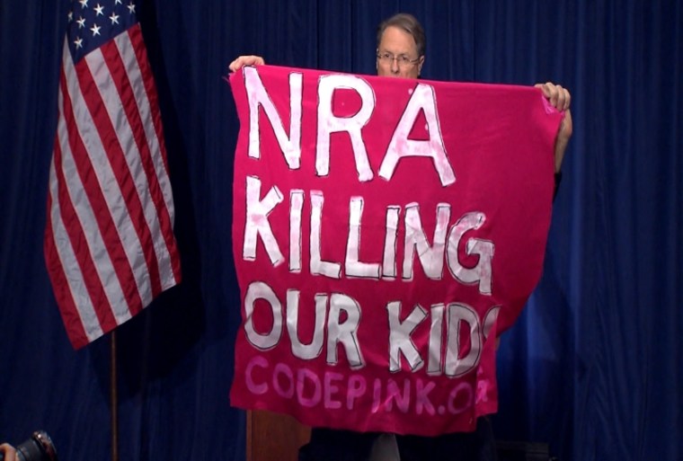 A protester holds up a sign as National Rifle Association executive vice president Wayne LaPierre speaks during a news conference in response to the Connecticut school shooting on Friday, Dec. 21, 2012 in Washington.