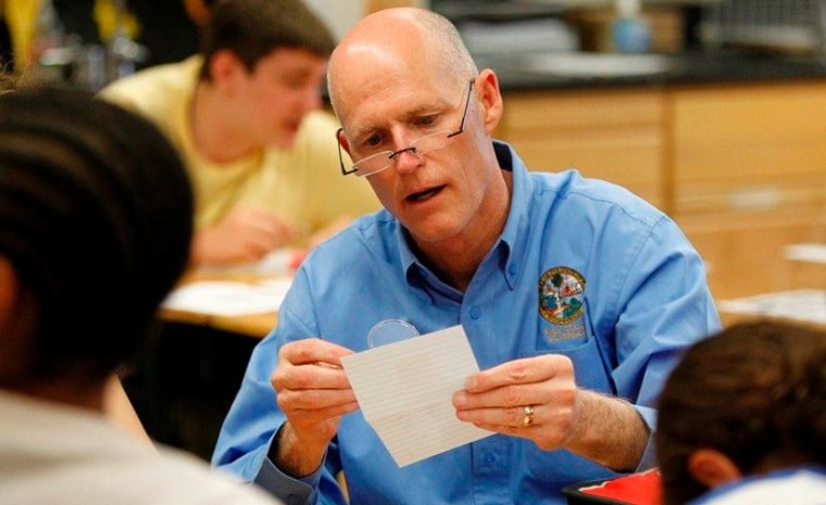 Florida Gov. Rick Scott uses a magnifying glass to look at finger prints in an 8th grade science class at Carwise Middle School in Palm Harbor, Fla., April 9, 2012.