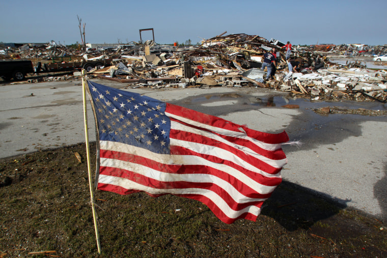 A torn and muddied American flag flies outside a boiler company as employees search through the wreckage of their office on the east side of Joplin, MO.  The workers said the flag was not theirs, but that they had found it in the building's debris,...
