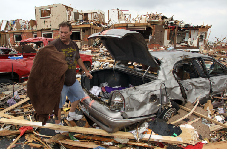 Ronnie Wilson pulls items from the trunk of his damaged car at an apartment complex in Joplin.  Wilson and his fiancee survived the tornado in the apartment at rear of the photo by huddling in the unit's bathroom.