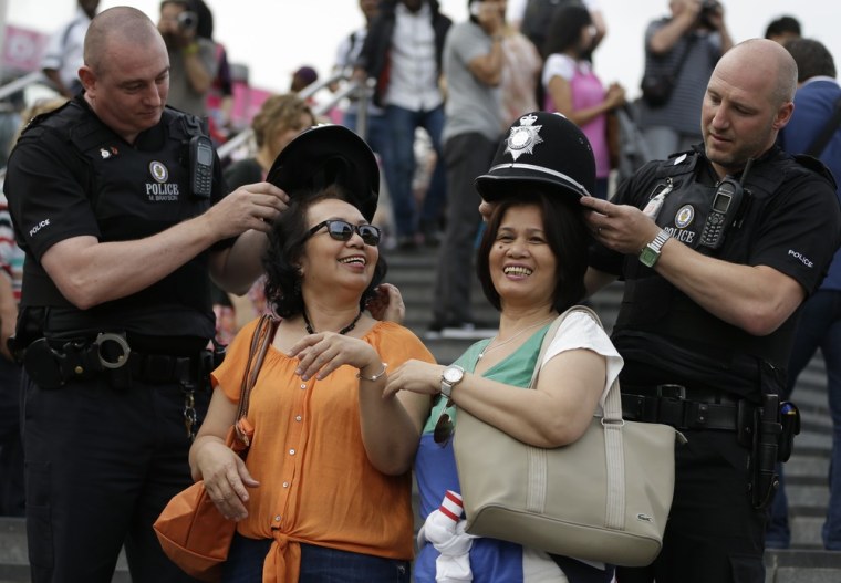 Police officers place their hats on Cynthia Sison, left, and Mercy Mesina, both of the Philippines, outside Olympic Park before the opening ceremony on July 27.