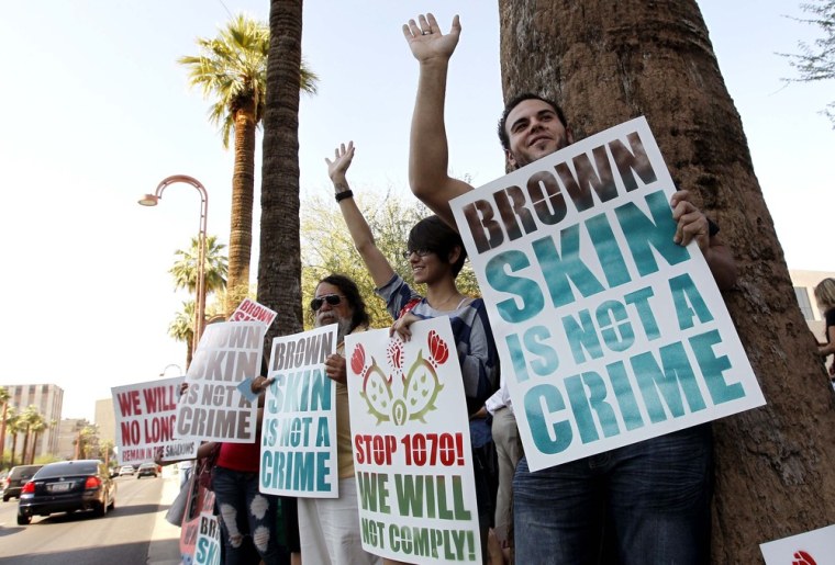 Laurent Taillefer, right, and Andrea Begay, second from right, both of Phoenix, wave at cars as they honk their horns driving by as the two join immigration rights protesters as they gather after the Supreme Court decision regarding Arizona's...