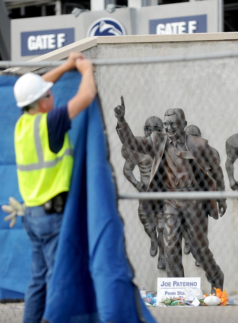 A worker hangs a blue tarp over the fence that was installed around the Joe Paterno statue. The university announced Sunday that it was taking down the monument in the wake of an investigative report that found that the late coach and three other top...