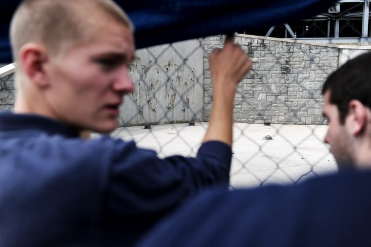 To get a clear view, Penn State students lift the tarp on the fence that blocks the site of the former Penn State University football coach Joe Paterno statue after it was removed by workers outside Beaver Stadium.