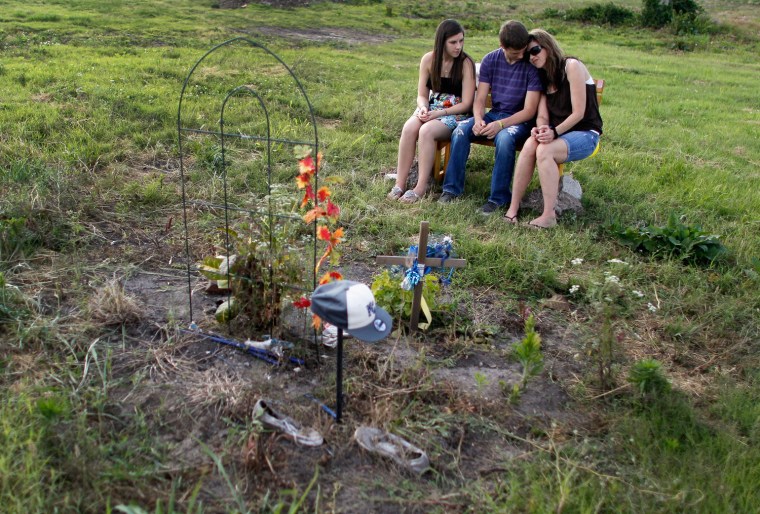 From left, Morgan Osburn, David Hoosier and Kim Hoosier spend a quiet moment together in front of a memorial built for their friend Lance Hare who was killed by a tornado that hit Joplin, Mo. a year ago.