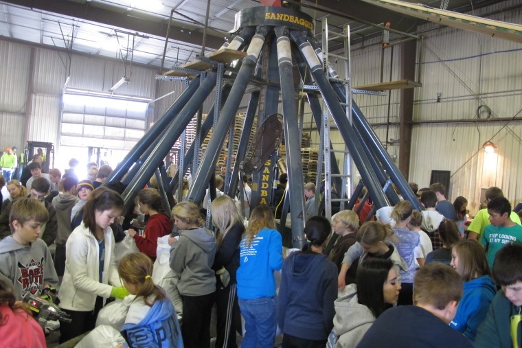 Students from Discovery Middle School in Fargo, N.D., help tie and stack sandbags around a \"Spider\" machine that has 12 funnels and can produce 5,000 bags an hour, during operations at Sandbag Central, Wednesday, April 3, 2013. (AP Photo/Dave Kolpack)