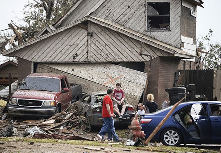 People are seen next to a damaged house and vehicles along a street after a huge tornado, in Moore, Oklahoma May 20, 2013. A 2-mile-wide (3-km-wide) tornado tore through the Oklahoma City suburb of Moore on Monday, killing at least 51 people while...