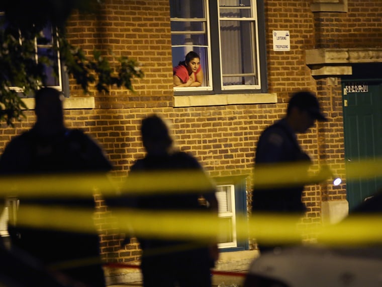 A woman watches from her window as police look for evidence after 20-year-old Carlos Barron was shot and killed in the Humboldt Park neighborhood on July 19, 2013 in Chicago, Illinois. (Photo by Scott Olson/Getty Images)